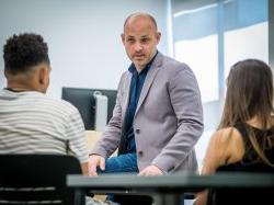 professor leaning on desk speaking to students